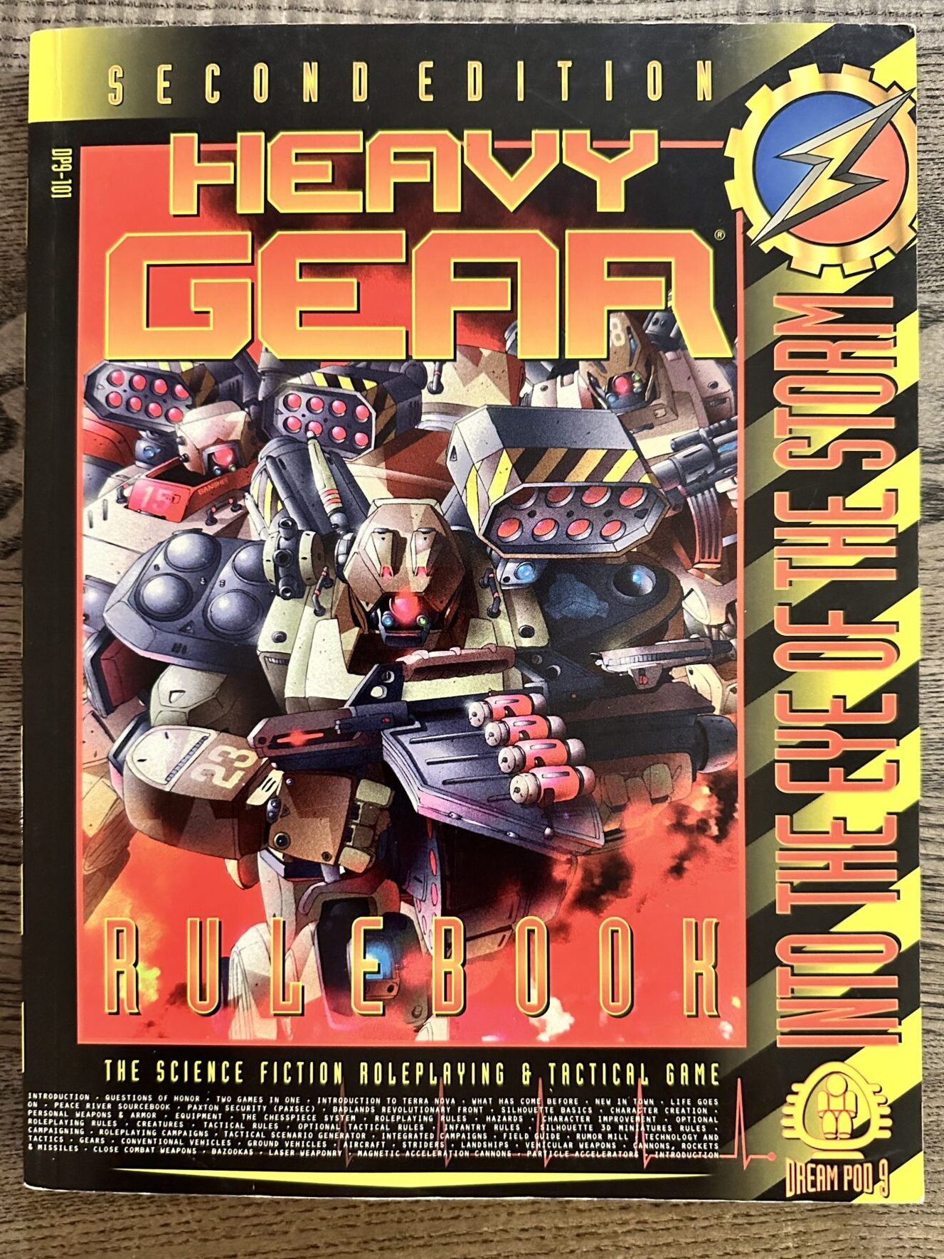 Heavy Gear roleplaying game, second edition, rulebook cover by Dream Pod 9 (1997). Ir depicts a group of giant robots advancing through the flames of a battle.