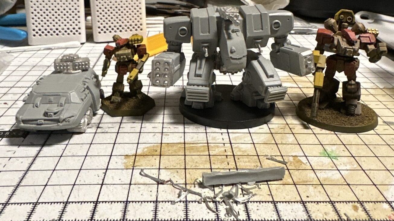 Heavy Gear miniatures on a craft table, in various stages of completion. Badger APC, Hunter Heavy Gear, Mammoth Strider, Kodiak (or Grizzly?) Heavy Gear.